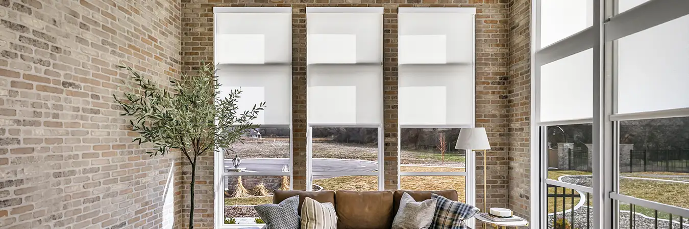 White motorized roller shades in a stylish living room with brick walls