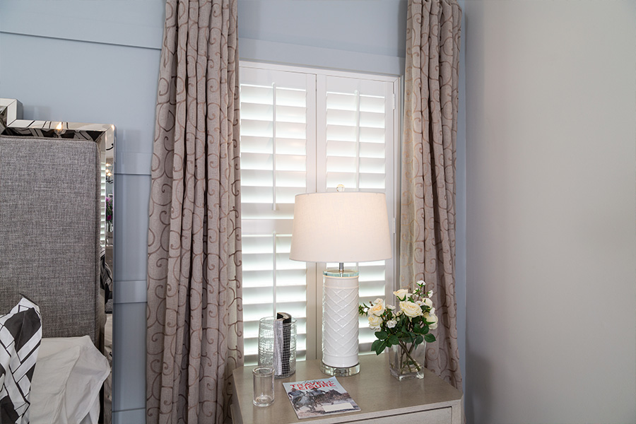 Layering curtains over white plantation shutters can make your windows look larger. white plantation shutters with curtains over small window in a bedroom