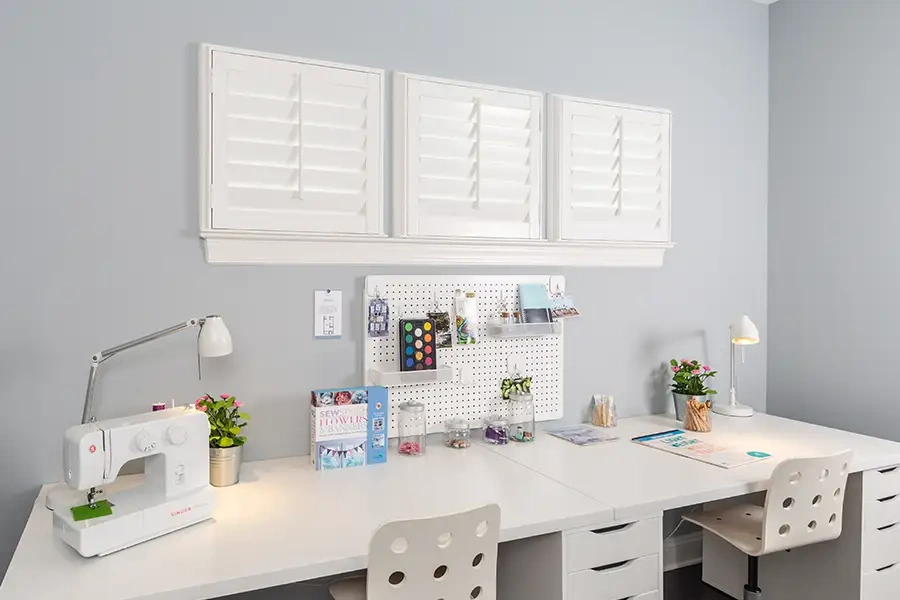 3 small white shutters in a row above a craft and art desk area
