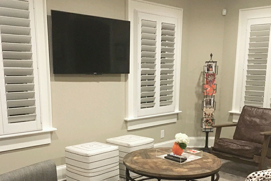 Put interior shutters in your media room to achieve the perfect amount of light or darkness. White Polywood shutters on windows in a room with a TV on the wall